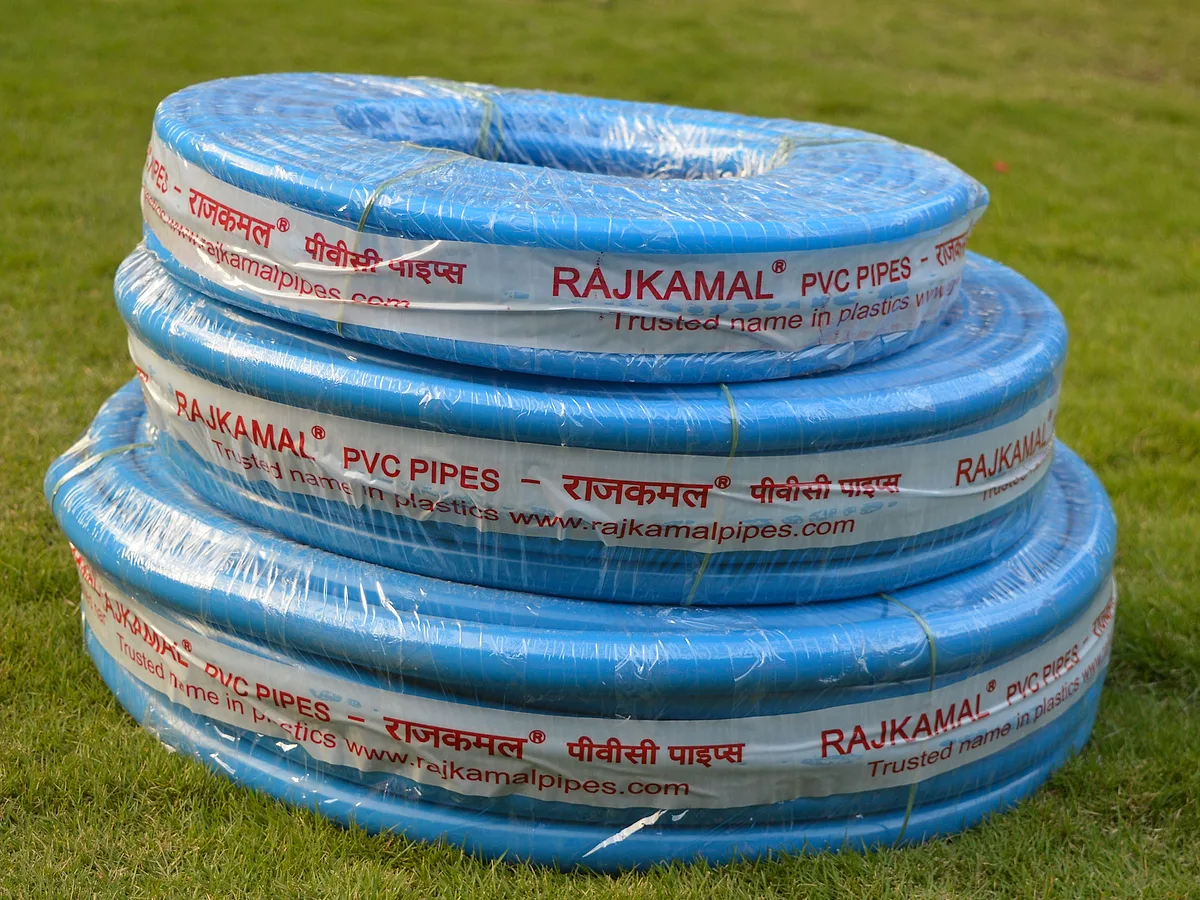Coils of blue Rajkamal PVC pipe stacked on grass